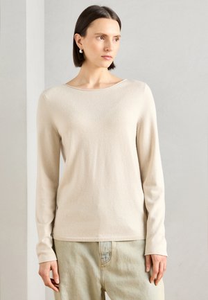 Lys beige langermet genser med en jevn tekstur og rund hals, kombinert med lyse jeans. Enkelt design uten mønstre eller dekorasjoner.