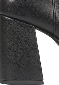 Black leather heeled boot with a textured surface. Features a chunky, rectangular heel and a smooth finish along the shaft.