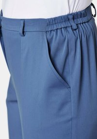 Blaue Hose mit elastischem Bund, seitlichen Taschen und glatter Textur, die eine lockere Passform und subtile Nähte aufweist.