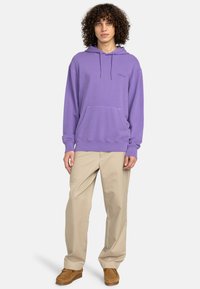 Lila hoodie med en framficka i kangoroo-stil, dragsko på huvan och ribbade ärmar. Bärs med beige byxor och bruna slip-on skor.