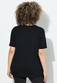 Camiseta negra de manga corta con cuello redondo, fabricada en una tela suave. La parte trasera tiene un corte relajado y es lisa, sin diseños visibles.