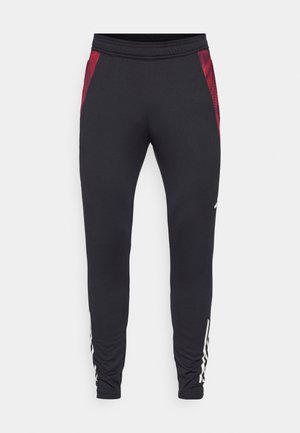 Fekete sportnadrág texturált piros oldalsó panelek, testhezálló fazon és elasztikus derékpánt jellemzi. Az alsó lábszáron fehér logó található.