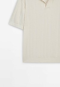 Polo en maille crème à manches courtes avec rayures verticales côtelées et petite ouverture de col sur fond blanc.