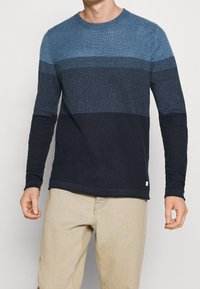 Långärmad skjorta med rundad halsringning som har gradientränder i mörkblått, ljusblått och marinblått. Texturerat tyg med en solid svart fåll.