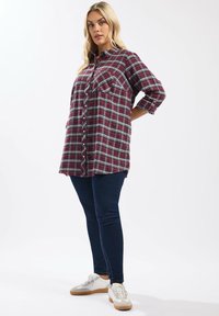 Rutig flanellskjorta i vinröd med knappstängning fram, två bröstfickor och uppvikta ärmar. Bärs med marinblå tajta jeans och vita sneakers.