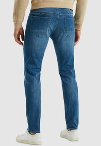 Slim-fit blauwe denim jeans met achterzakken, lichte vervaging en een gladde textuur, gecombineerd met witte sneakers.