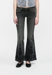 Μαύρο τζιν με καμπάνα, διακοσμημένο με floral κέντημα στο τελείωμα, με πέντε τσέπες και ελαφρώς ξεθωριασμένη όψη.