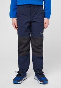Pantaloni impermeabili blu navy con un pannello grigio scuro a contrasto, vita elastica e polsini regolabili, abbinati a scarpe da ginnastica blu.