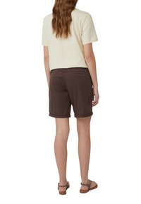 Bruine omgerolde shorts van lichtgewicht stof, gecombineerd met een crèmekleurig t-shirt. De outfit wordt compleet gemaakt met platte sandalen.