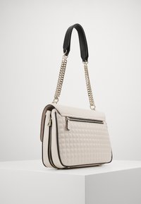 Kremowa pikowana torebka z złotym łańcuszkiem i czarną poduszką na ramię. Posiada przednią kieszeń na suwak oraz kontrastowe czarne wykończenie. Prostokątny kształt.