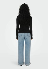 Schwarzes geripptes Langarmoberteil mit gewelltem Saum, kombiniert mit hellblauen weiten Jeans, die umgeschlagene Bündchen und Gesäßtaschen haben.