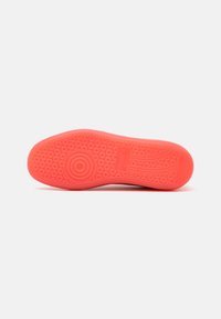 Suela de zapatilla de goma rosa con patrones de tracción circulares, un acabado texturizado y una sección de talón suave. Marca mínima visible.