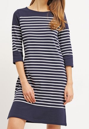 Frau trägt ein marineblaues Kleid mit weißen horizontalen Streifen, dreiviertel Ärmeln und einem einfarbigen marineblauen Saum.