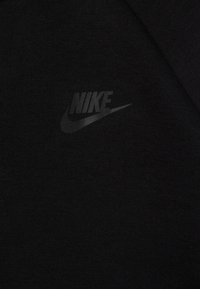 Black sweatshirt made of textured fabric featuring a subtle, dark Nike logo on the left side. Simple design with a crew neckline.