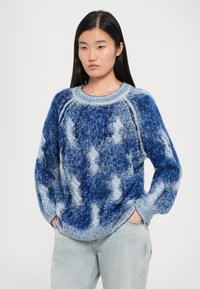 Pulover tricotat în nuanțe de albastru, cu un model texturat în diamante, mâneci largi și guler rotund. Purtați peste blugi deschiși la culoare.