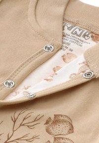 Beige Body aus Bio-Baumwolle mit Fischmuster. Druckknöpfe am Halsausschnitt. Weicher Stoff mit bedruckten Details.