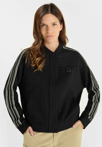 Svart tröja med ränder, med ståkrage och långa ärmar med vita ränder. Inkluderar en framficka och subtil logotypdetalj.