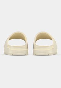 Kremowe klapki na płaskiej podeszwie, z odkrytym tyłem, gładką fakturą oraz lekko podniesioną podeszwą z wzorem antypoślizgowym na spodzie.