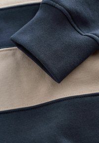 Navy and beige cotton sweatshirt fabric, featuring horizontal stripes and a folded cuff, with visible stitching details and a soft texture.