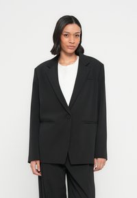 Zwarte oversized blazer met een enkele knoop, revers met inkeping en twee voorzakken. Soepele stof met een matte afwerking en een getailleerd ontwerp.