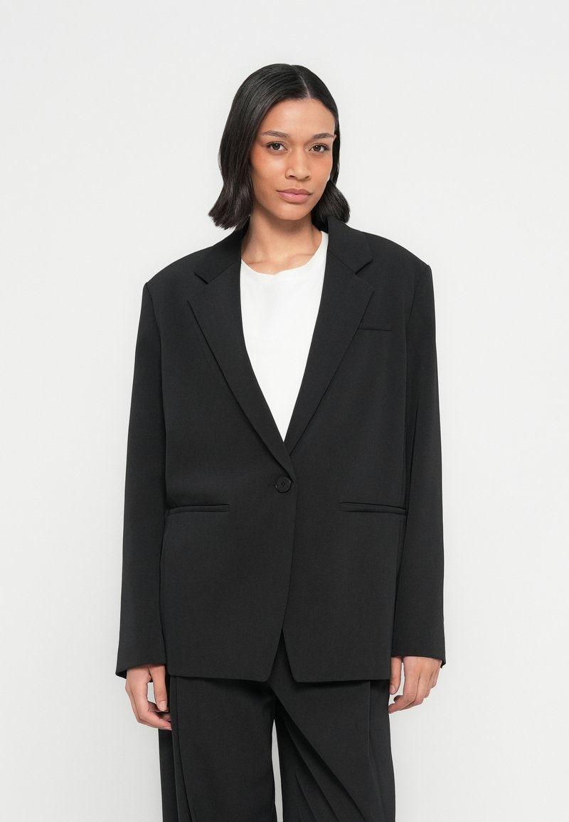 Zwarte oversized blazer met een enkele knoop, revers met inkeping en twee voorzakken. Soepele stof met een matte afwerking en een getailleerd ontwerp.