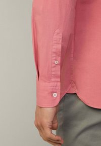 Camisa de manga larga en algodón rosa claro con puños de botón, con detalles de botones en contraste y un dobladillo curvado.