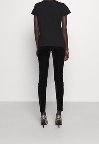 Camiseta negra de manga corta combinada con pantalones de terciopelo negro ajustados y zapatos de tacón alto con estampado, vista desde atrás.