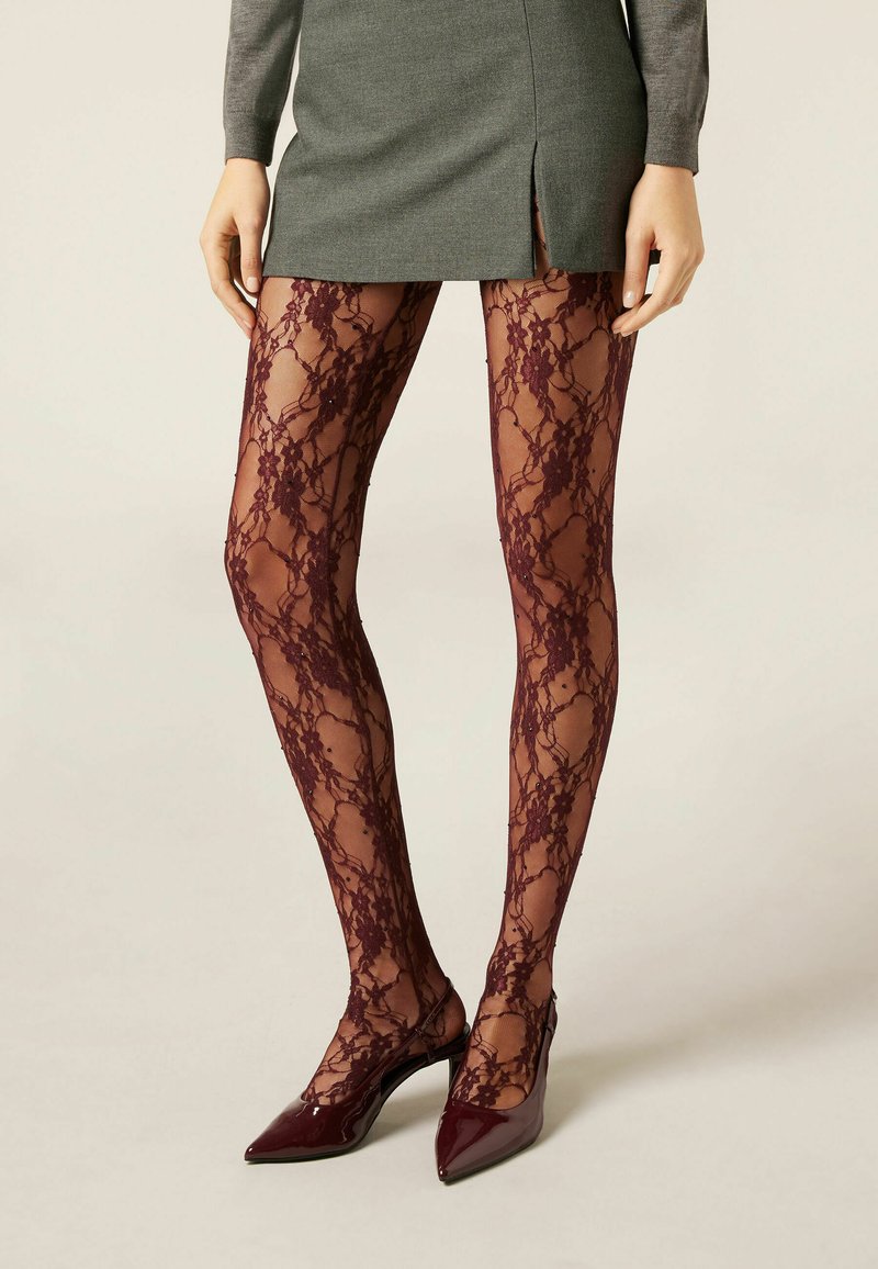 Bordeaux blonde tights med blomsterdesign og en gennemsigtig finish, båret med en grå nederdel og spidse patenthæle for kontrast.