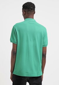 Grön polo skjorta i texturerad tyg, med klassisk krage och korta ärmar. Bakifrån visas en rak nederkant och avslappnad passform.