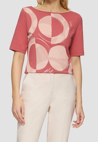 Röd och rosa kortärmad topp med cirkulära och abstrakta former, gjord av mjukt tyg, med en båtkrage och subtila grafiska detaljer.