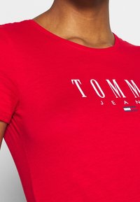 Czerwona bawełniana koszulka z okrągłym dekoltem, z napisem "TOMMY JEANS" w białym kolorze oraz małym logo w czerwonych, białych i niebieskich akcentach.