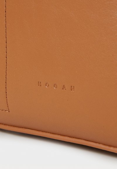 Tan leather bag featuring a smooth texture, subtle stitching, and embossed "HOGAN" logo. Minimalist design with no additional hardware or accents.