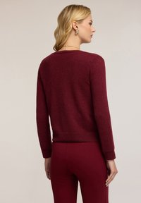 Burgundské svetr s dlouhými rukávy, kulatým výstřihem, žebrovanými manžetami a lemem. Měkká textura, v kombinaci s odpovídajícími upnutými kalhotami.