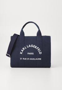 Mörkblå tygkasse med dubbla handtag, justerbar axelrem och vit text "KARL LAGERFELD PARIS 21 RUE ST-GUILLAUME" på framsidan.