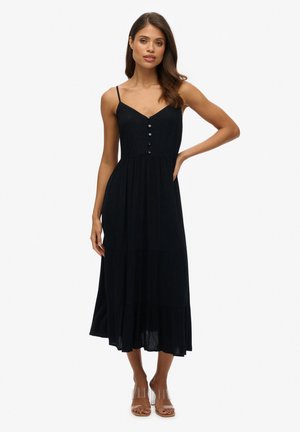 Vestido maxi negro con tirantes finos, cuerpo abotonado y falda de volantes. Hecho de un tejido ligero con una textura suave. Sandalias de tacón transparente.