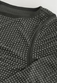 Top nero strutturato con borchie metalliche argento disposte uniformemente sulla stoffa, con scollatura liscia e orlo curvo.