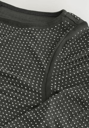 Mustra mustriga must top, millel on metallist hõbedased nurgad, mis on ühtlaselt paigutatud riidetükile, ning sujuv kaelus ja kõver hem.