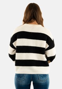 Maglione a righe bianche e nere con una texture morbida, scollo rotondo e spalle abbassate. Indossato sopra un paio di jeans blu.