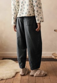 Kockás fekete-fehér nadrág, laza fit, virágmintás pulóverrel és puha, bolyhos papuccsal viselve.