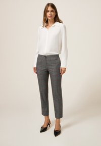 Camicia bianca con bottoni e maniche lunghe abbinata a pantaloni a quadri grigi con accenti rossi, completata da tacchi a punta neri.