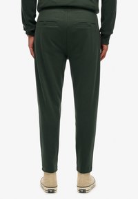 Grønne sweatpants med en tætsiddende pasform, som har to baglommer og en glat tekstur. Båret med beige høje sneakers.