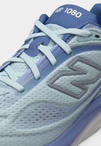 Παπούτσι για τρέξιμο New Balance 1080 σε ανοιχτό μπλε και λιλά, με υφασμάτινη διχτυωτή επιφάνεια, ανοιχτό μπλε κορδόνια και το λογότυπο "N" της μάρκας στο πλάι.