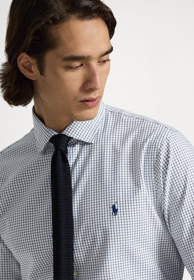 Λευκό ανδρικό πουκάμισο με ναυτικό μπλε καρό σχέδιο, γιακά με κουμπιά και κεντητό λογότυπο. Συνδυασμένο με υφασμένη σκούρα γραβάτα.