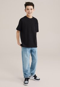 Svart bomullströja med bröstficka, kombinerad med ljusblå denimjeans och svarta sneakers med grå accenter.