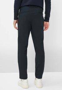 Donkerblauwe broeken met een slim fit, gemaakt van gladde stof, voorzien van twee achterzakken en een strakke zoom, gedragen met witte sneakers.