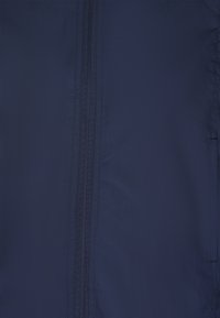 Mörkblått tyg med en slät textur, som har två parallella dragkedjor längs mitten. Materialet verkar lätt och hållbart.
