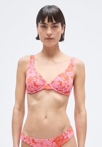 Pink floral bikini top with a triangular shape, adjustable straps, and textured fabric. Features a twisted center design and matching bottom.
