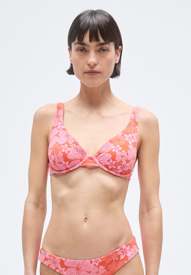 Pink floral bikini top with a triangular shape, adjustable straps, and textured fabric. Features a twisted center design and matching bottom.