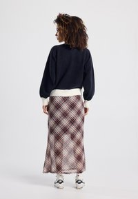 Navy Pullover mit Ballonärmeln, cremefarbener gerippter Saum, kombiniert mit einem transparenten, karierter Maxirock in Beige-, Burgundy- und Cremetönen. Schwarze Sneaker.
