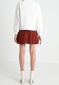 Weißer strukturierter Pullover, bordeauxroter Wildleder-Minirock und weiße Absatz-Stiefeletten. Das Outfit hat eine lockere Passform und minimalistisches Design.